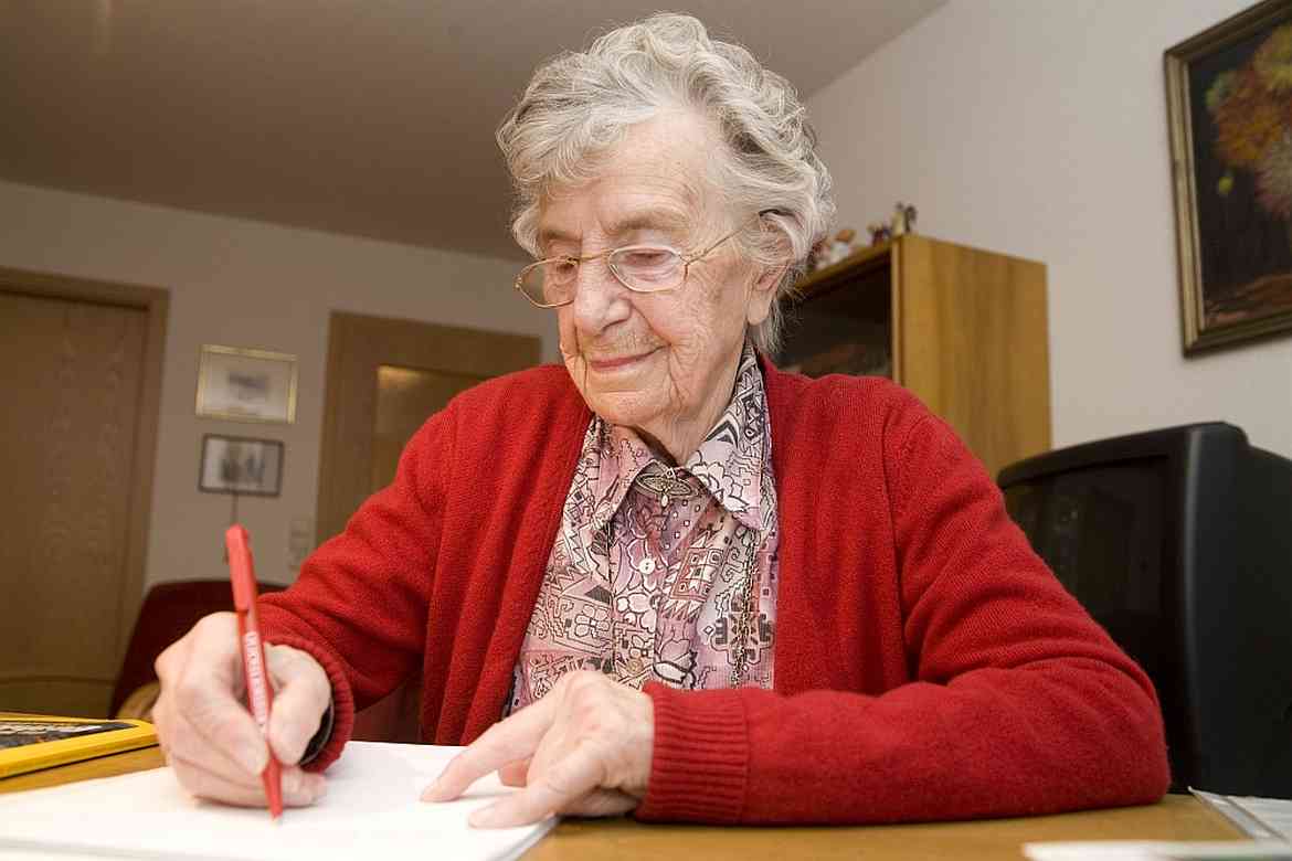 Eine ältere Dame sitzt am Schreibtisch und verfasst ihre Patientenverfügung.