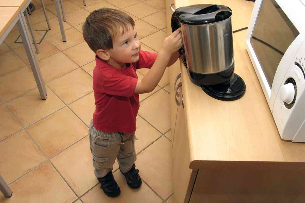Ein kleiner Junge greift nach einem Wasserkocher.