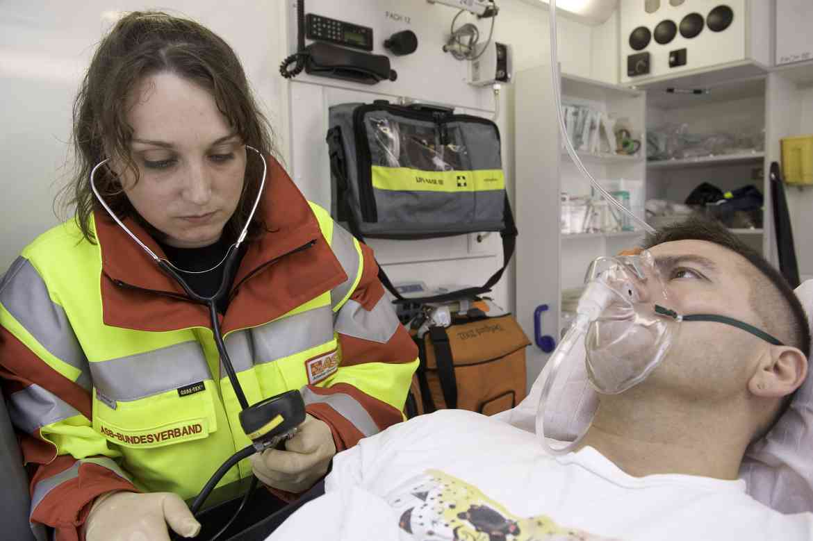 Patient mit Sauerstoffmaske wird der Blutdruck von einer Rettungssanitäterin im Rettungswagen gemessen.