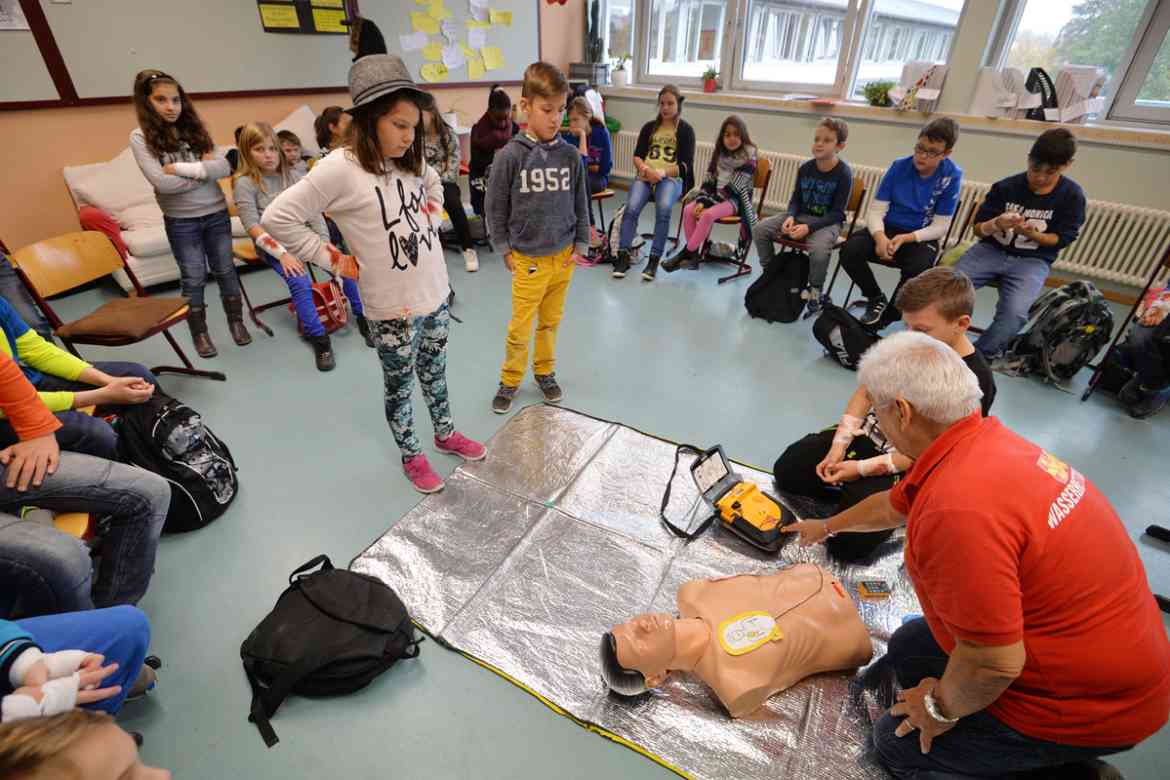 Ein ASB-Ausbilder schult in einer Schulklasse Lehrer und Schüler in Erster-Hilfe.